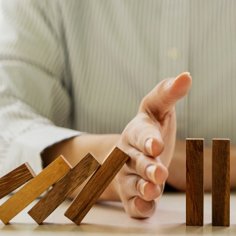 Ein Mann verhindert mit seiner Hand, dass Dominosteine umfallen