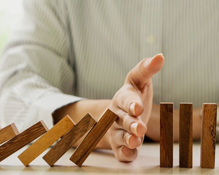 Ein Mann verhindert mit seiner Hand, dass Dominosteine umfallen