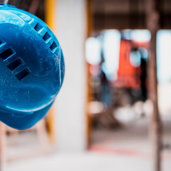 Ein blauer Helm hängt an einer Leiter vor einer Baustelle