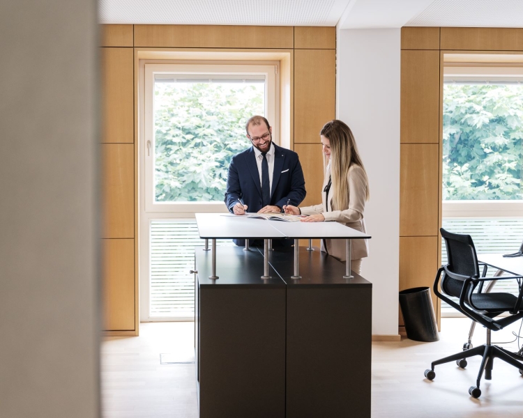 Ein Geschäftsmann und eine Geschäftsfrau unterhalten sich bei einem Stehtisch und betrachten Unterlagen