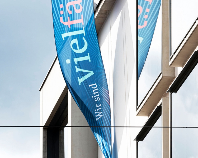 Eine blaue Flagge mit der Aufschrift Wir sind vielfältig an einem Gebäude angebracht