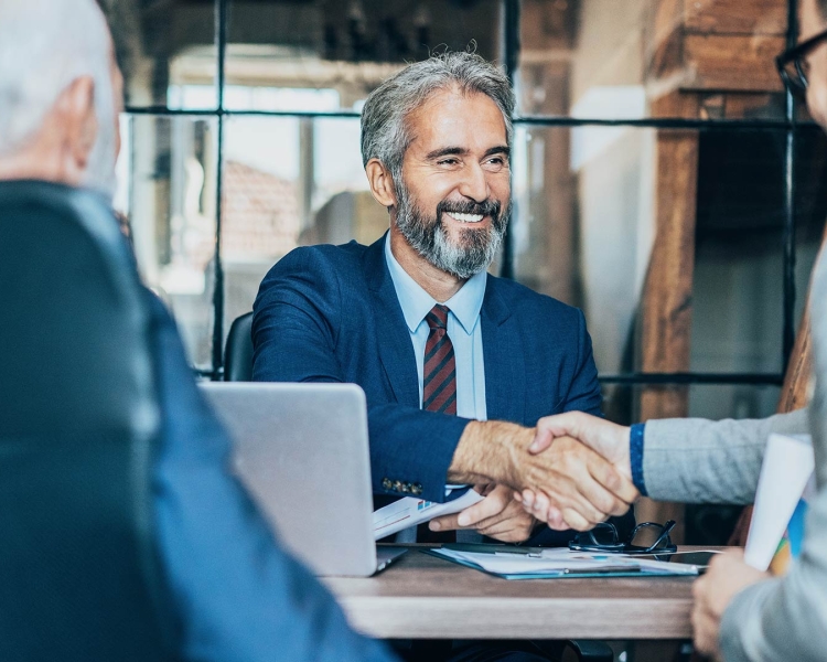 A man shakes the hand of another man while sitting at a table together
