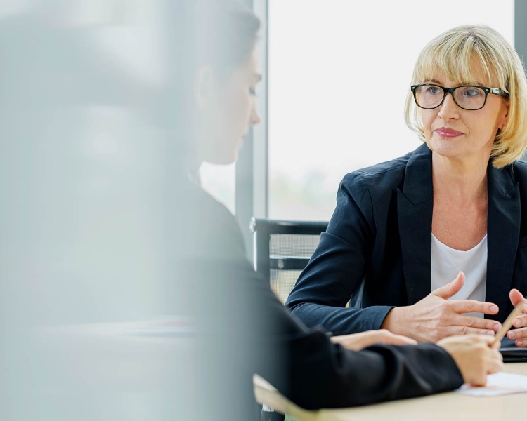 Two business ladies talk to each other while sitting at a table