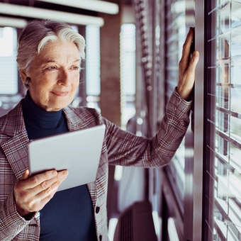 Eine Geschäftsfrau hält ihr Tablet in einer Hand und blickt aus dem Fenster