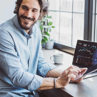 Ein Mann sitzt vor seinem Notebook und tippt auf sein Smartphone