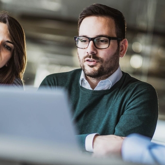 Drei Personen blicken gemeinsam auf den Bildschirm von einem Notebook