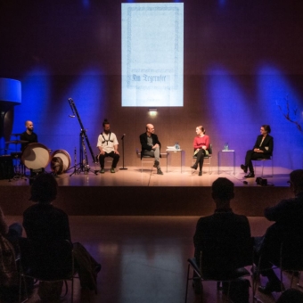 Fünf Personen sitzen auf einer Bühne und diskutieren, mehrere Personen verfolgen die Unterhaltung