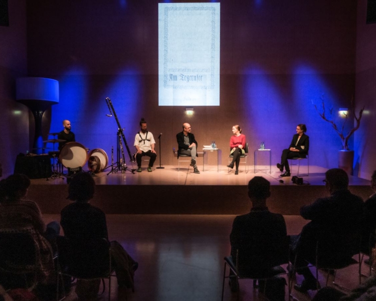 Fünf Personen sitzen auf einer Bühne und diskutieren, mehrere Personen verfolgen die Unterhaltung