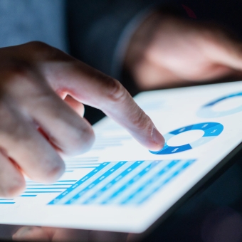 Eine Person tippt auf ihr Tablet und analysiert dabei ein Diagramm und eine Tabelle