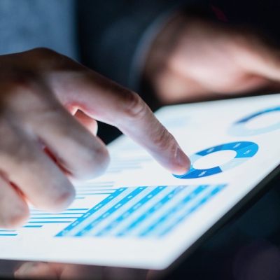 Eine Person tippt auf ihr Tablet und analysiert dabei ein Diagramm und eine Tabelle