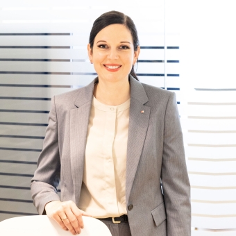 Eine Frau in einem grauen Anzug steht vor einer Glasfront