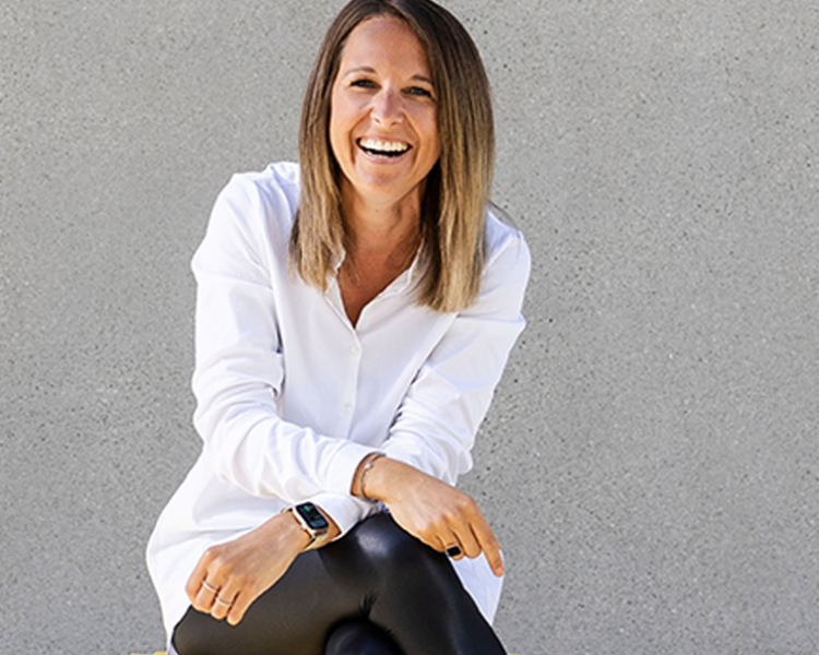 Eine Frau sitzt auf einem Hocker und lächelt in die Kamera