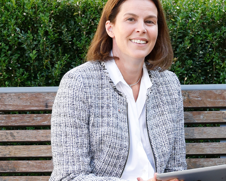 Ein Frau hält ein Tablet in der Hand uns sitzt auf einer Gartenbank