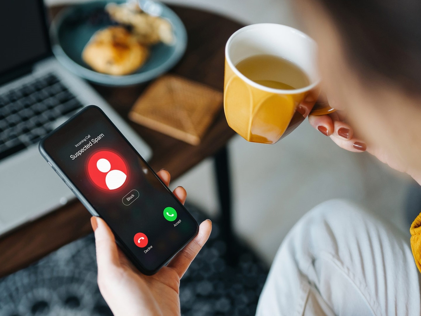 Eine Frau blickt auf ihr Smartphone, da eine unbekannte Nummer anruft und hält eine Tasse mit Kaffee in der anderen Hand