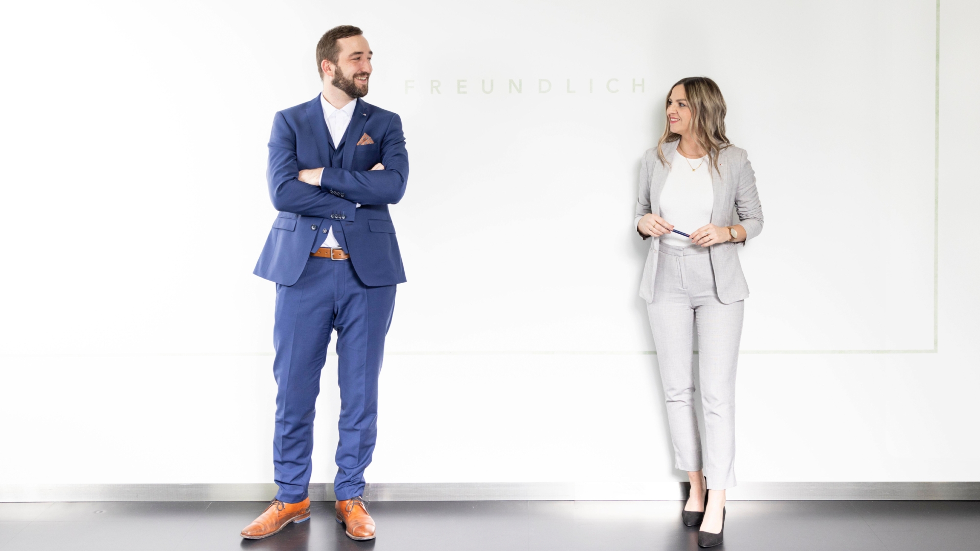 2 Personen in einem Anzug stehen vor einer weißen Wand und sehen sich an