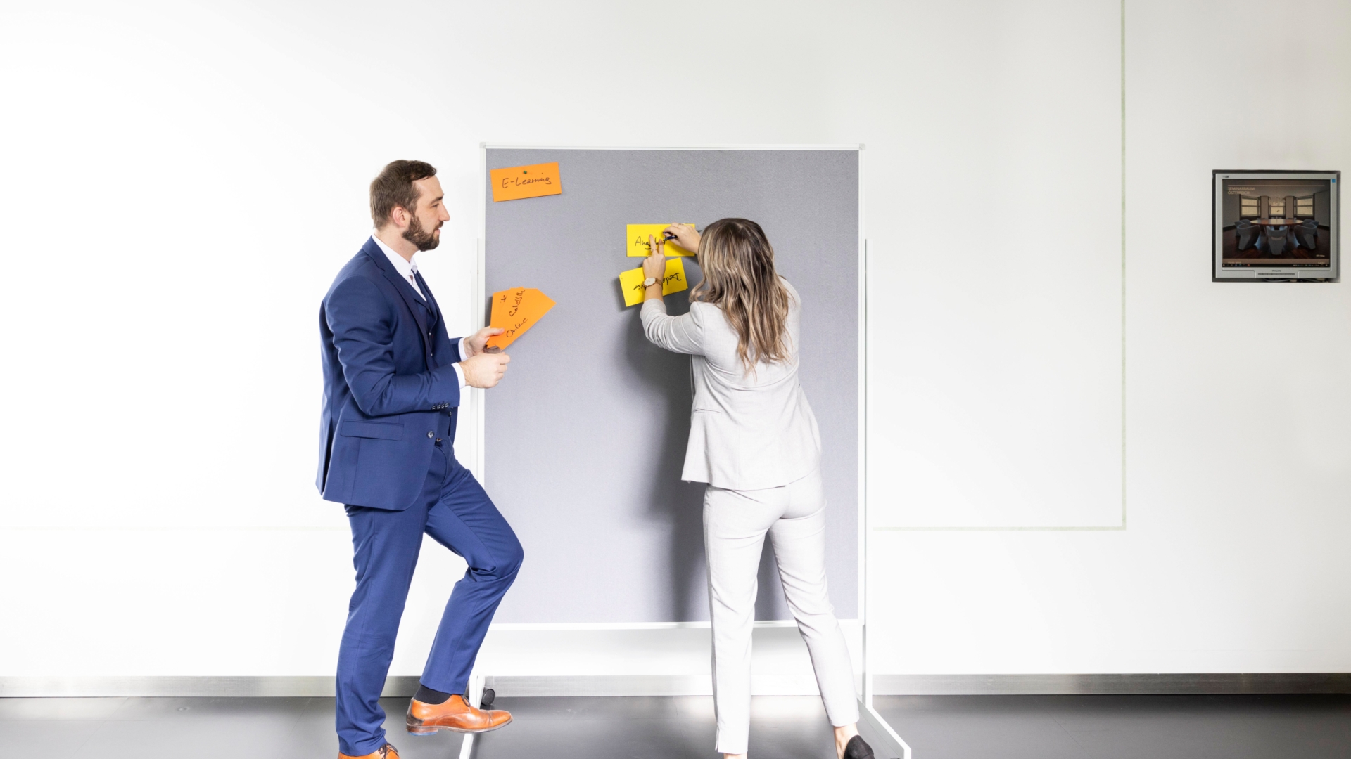 Frau und Mann, die bunte Kärtchen auf Pinwand anbringen