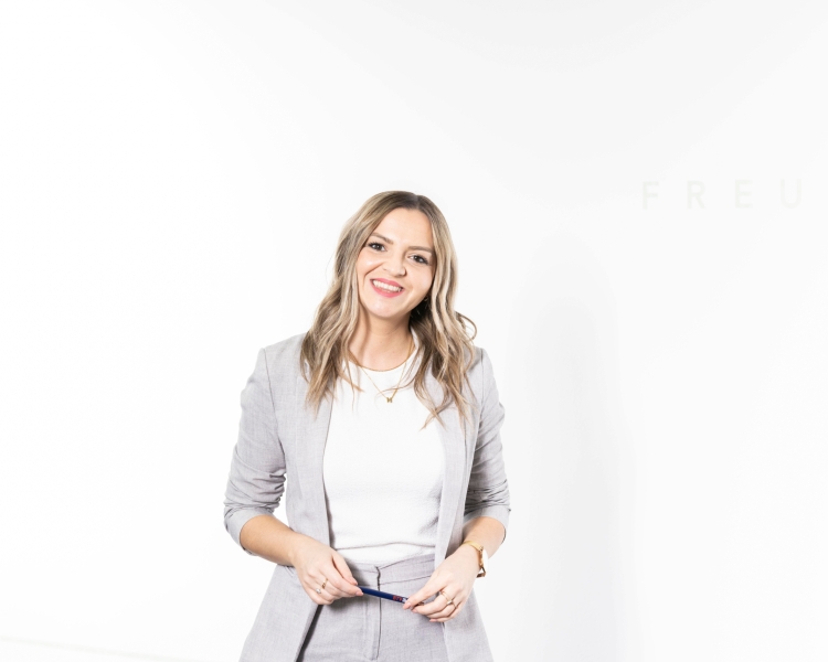 Eine Frau lächelt in die Kamera und trägt einen grauen Anzug