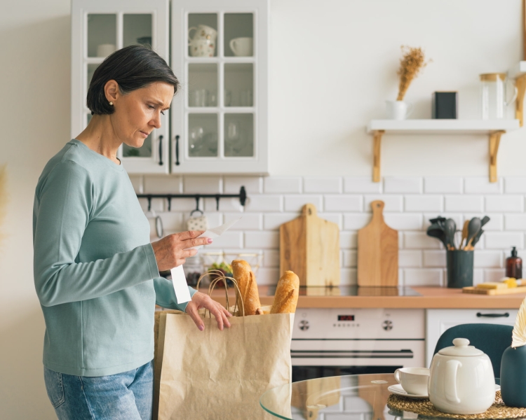 Eine Frau betrachtet frustriert den Kassabon in ihrer Küche nach dem Einkaufen im Supermarkt