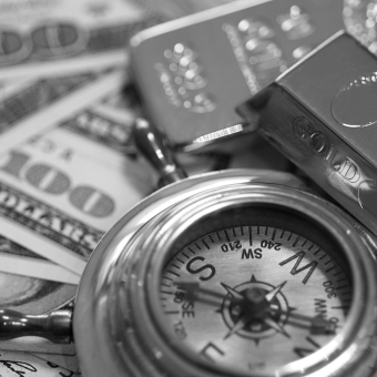 Ein antiker Kompass liegt auf Dollar-Scheinen, daneben befinden sich Goldbarren