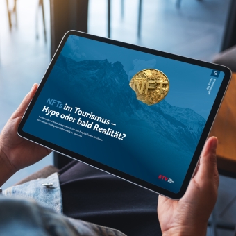 Tablet wird von zwei Händen gehalten. Darauf ist ein Foto mit dem Inhalt NFTs im Tourismus - Hype oder bald Realität? zu sehen.