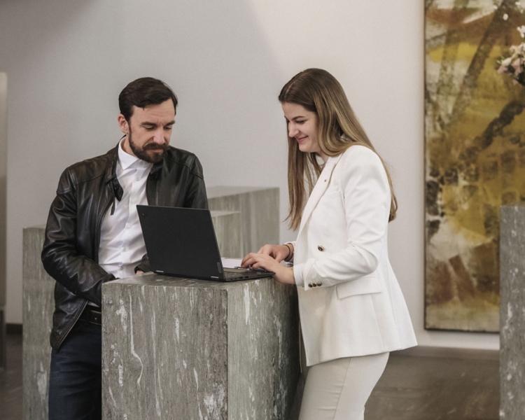 Zwei Personen stehen an einem Stehtisch und nutzen einen Laptop.