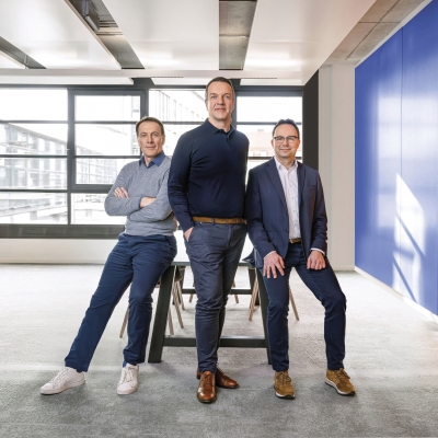 Geschäftsführung von NFON: Chief Product Officer (CPO) Markus Krammer, Chief Executive Officer/Chief Finance Officer (CEO/CFO) Patrik Heider, Chief Technology Officer (CTO) Andreas Wesselmann. Drei Herren in einem Besprechungszimmer an einen Tisch gelehnt, Fensterfront im Hintergrund.