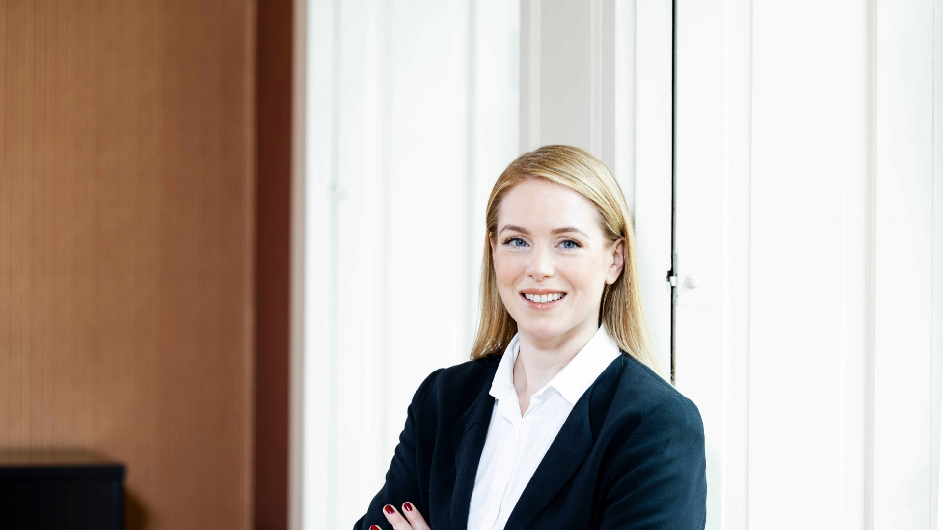 Eine Frau mit weißer Bluse und dunklem Blazer lächelt in die Kamera