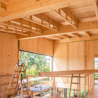 Ein Raum mit Holzwänden und Holzdecke, einem Baugerüst und großen Fenstern sowie drei Holzleitern und mehreren Holzlatten für die Sanierungsarbeiten