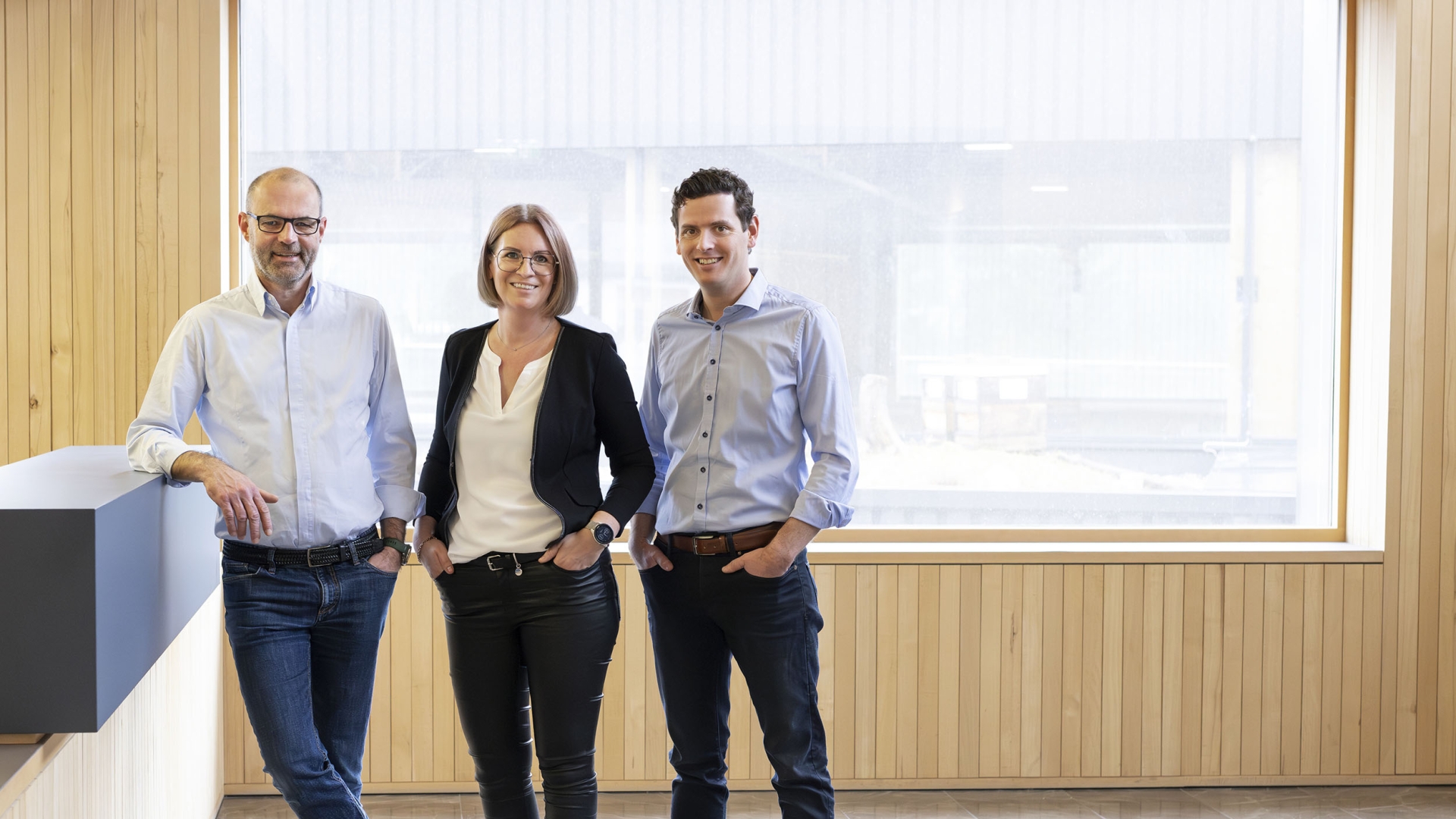 Zwei Männer und eine Frau stehen in einer Empfangshalle