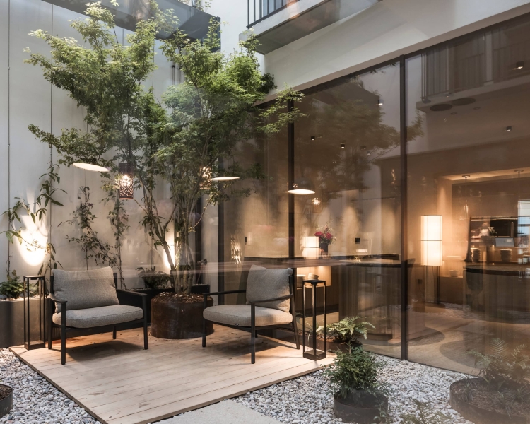 Lichthof mit vertikalem Garten im Boutique Hotel Eisenhut in Bozen: Zwei Gartenstühle stehen auf einem Holzboden, umgeben von grobem Kies. Grüne Pflanzen stehen großzügig verteilt im Lichthof.