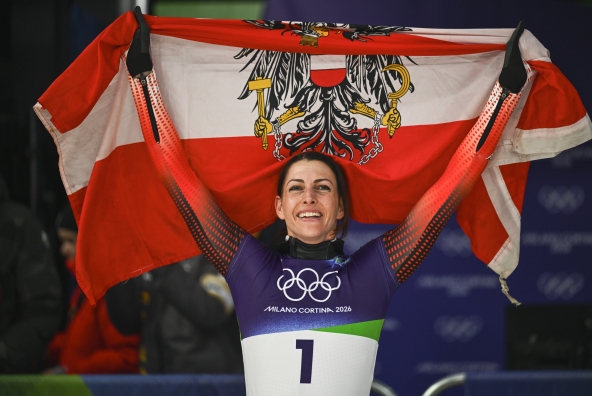 Skeletonpilotin Janine Flock hält eine Österreichflagge inkl. Tiroler Adler über ihren Kopf. Sie feiert ihre Goldmedaille auf den Olympischen Spielen in Milano Cortina 2026.