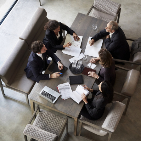 Fünf Geschäftsleute sitzen an einem Tisch zusammen und sprechen miteinander
