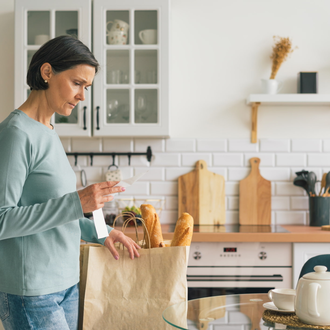 Frau betrachtet frustriert den Kassabon in ihrer Küche nach dem Einkaufen im Supermarkt