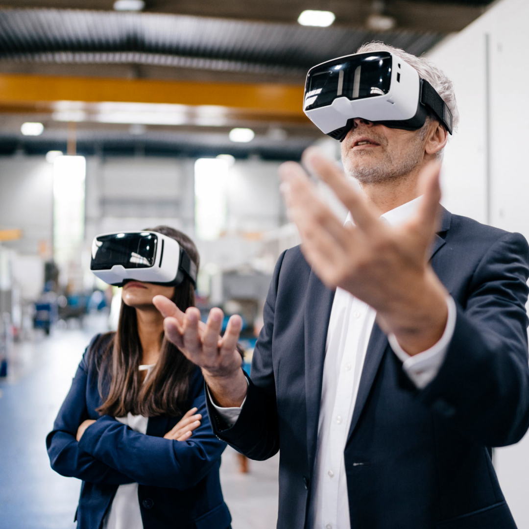 Eine Dame und ein Herr tragen eine eine Virtual Reality Brille. Der Herr hebt seine beiden Hände dabei.