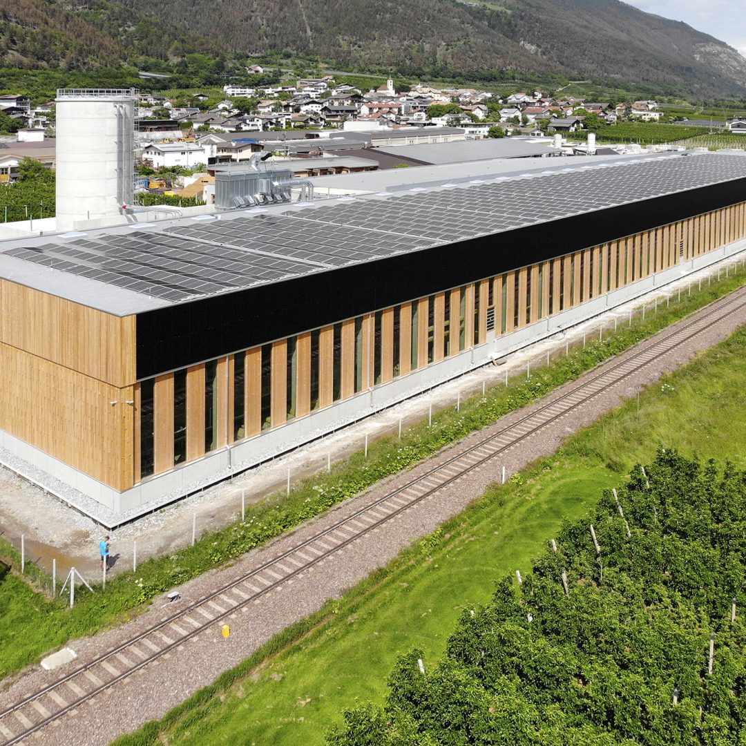 holzius-Firmensitz aus Holz mit Photovoltaikanlage auf dem Dach neben Bahnschienen