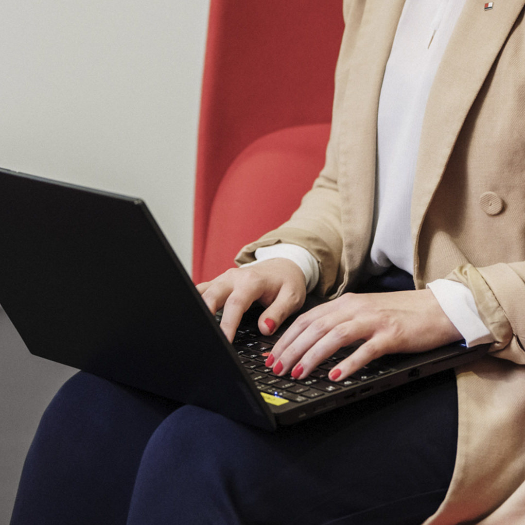 Eine Frau sitzt in einem roten Sessel und und arbeitet mit ihrem Laptop.