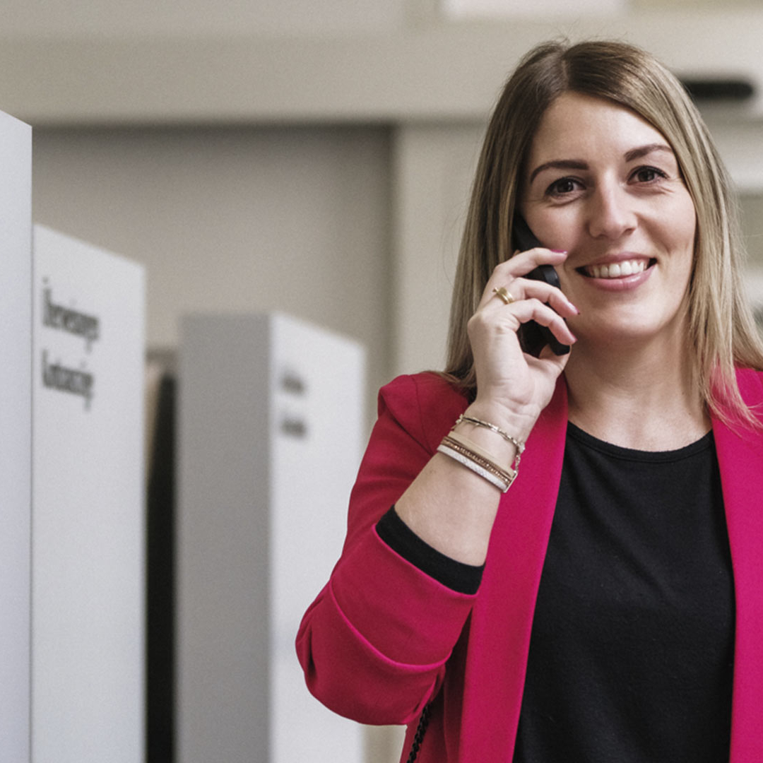 Eine Frau steht neben einem Bankomaten und telefoniert.